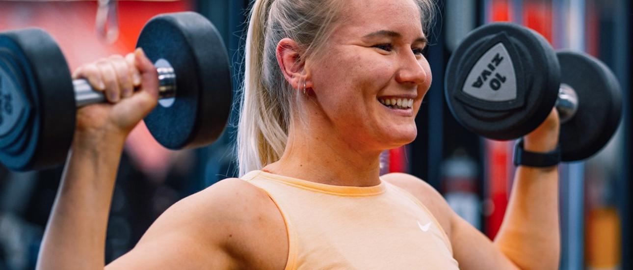Stark tjej som kör axelpress med vikter på ett Fitness24Seven gym