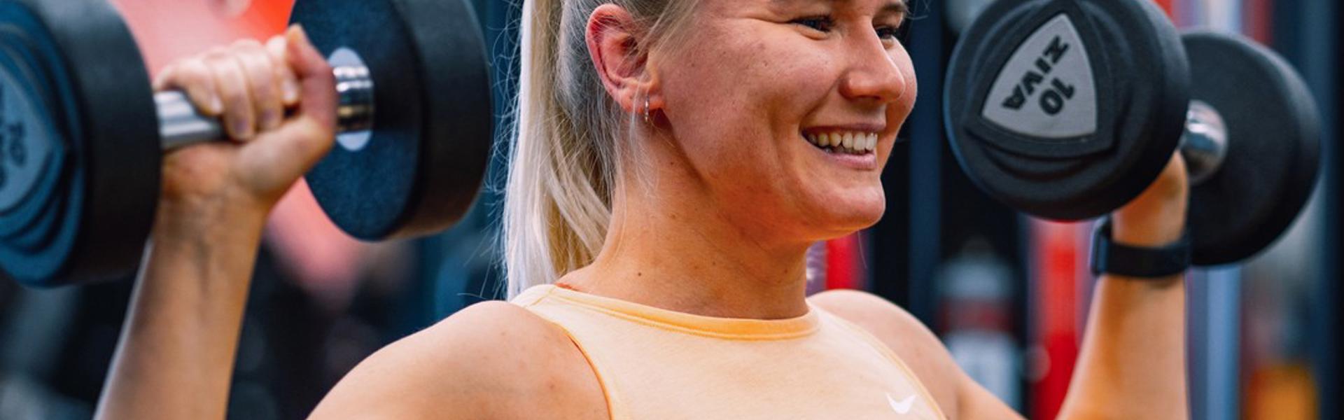 Stark tjej som kör axelpress med vikter på ett Fitness24Seven gym