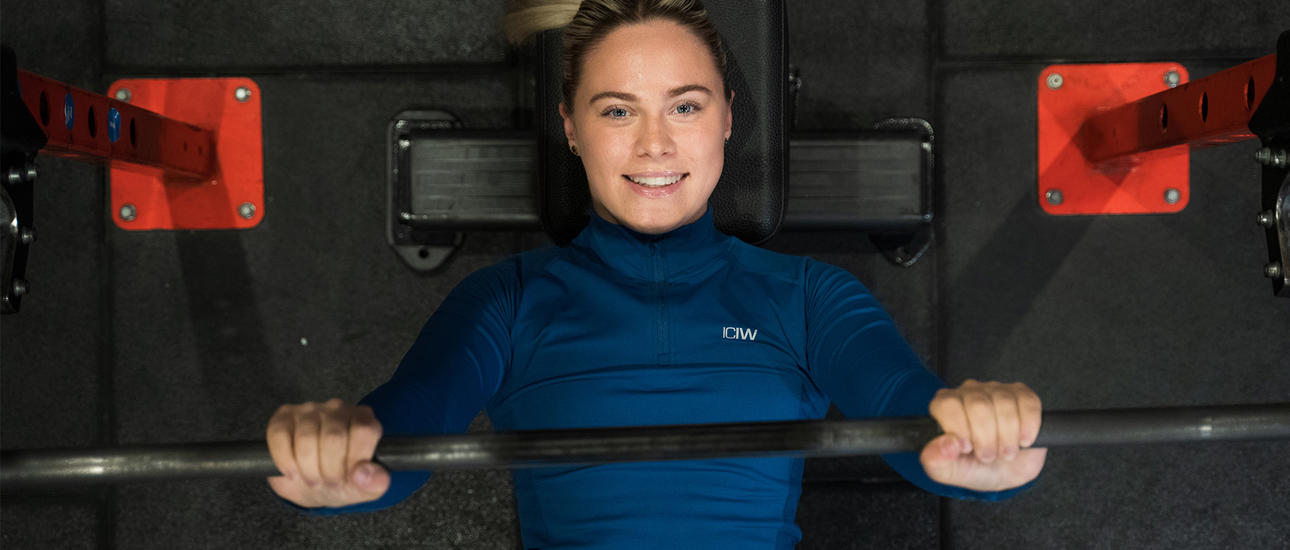 Kvinna kör skivstång liggande på gymmet