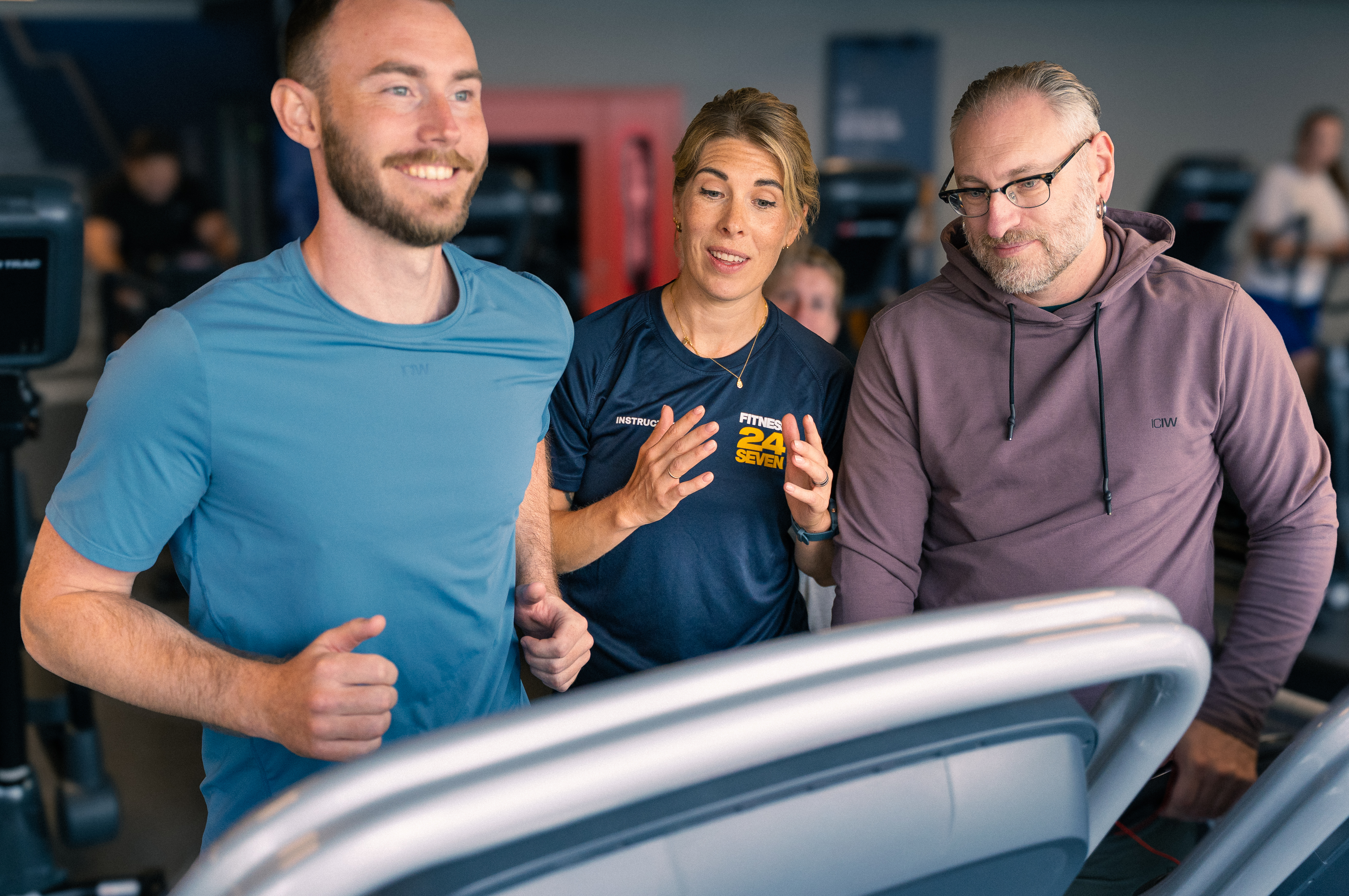 Man springer på löpband, två personer står bredvid och hejar på