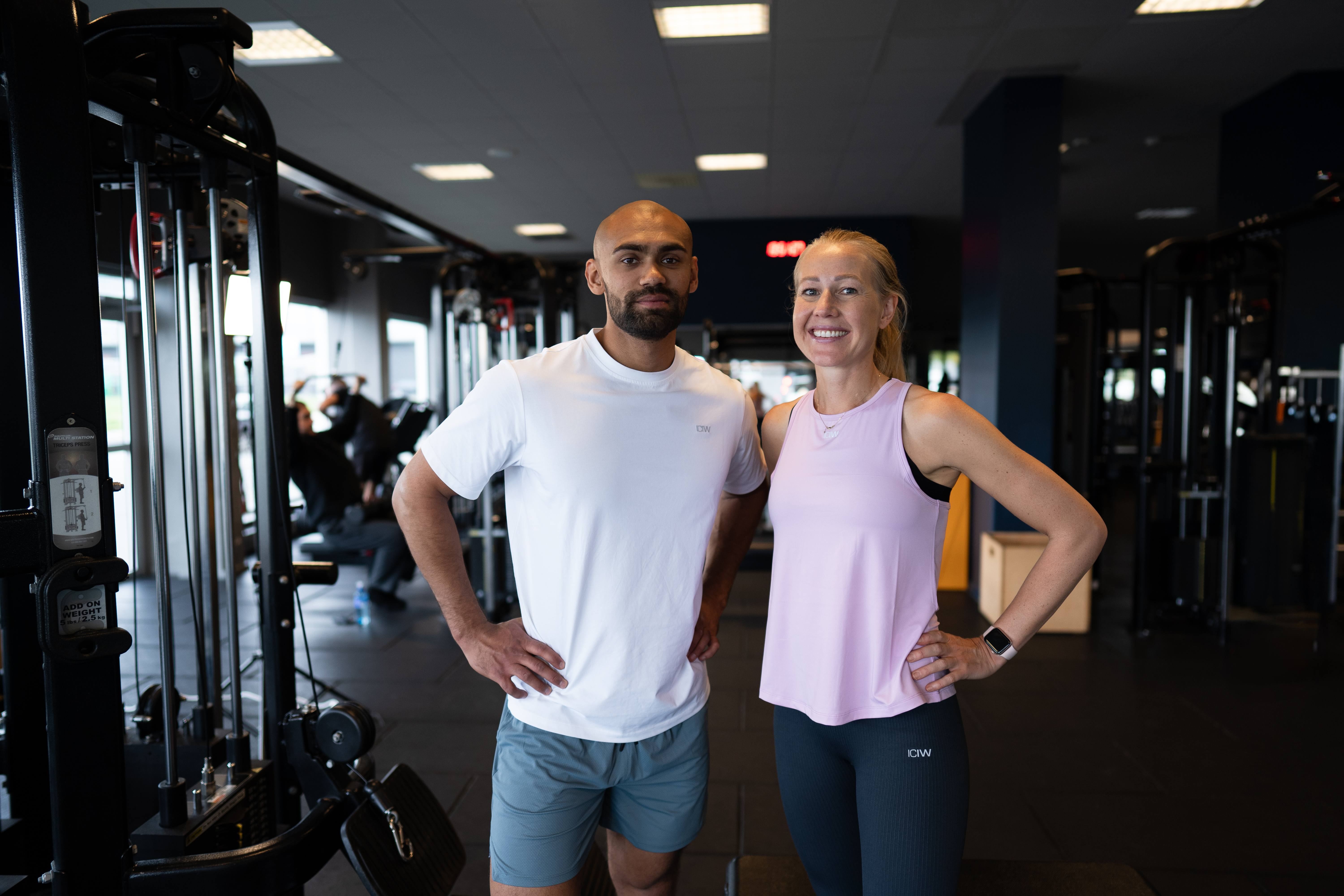En manliga och kvinnlig medlem ler och tittar in i kamera på gym